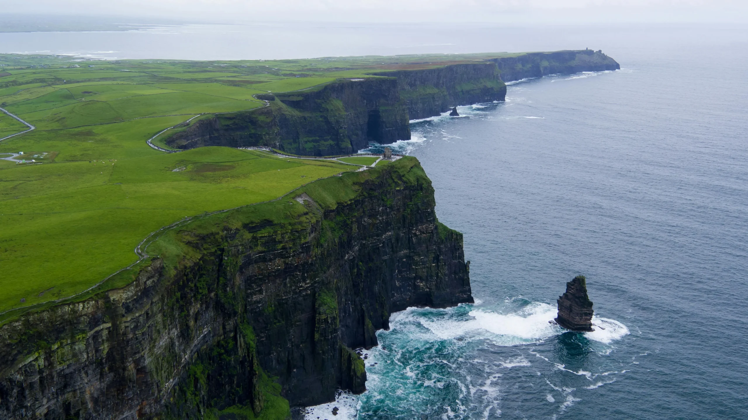 Aerial view of the Cliffs of Moher in Ireland, showcasing lush green fields leading to steep cliffs dropping into the Atlantic Ocean